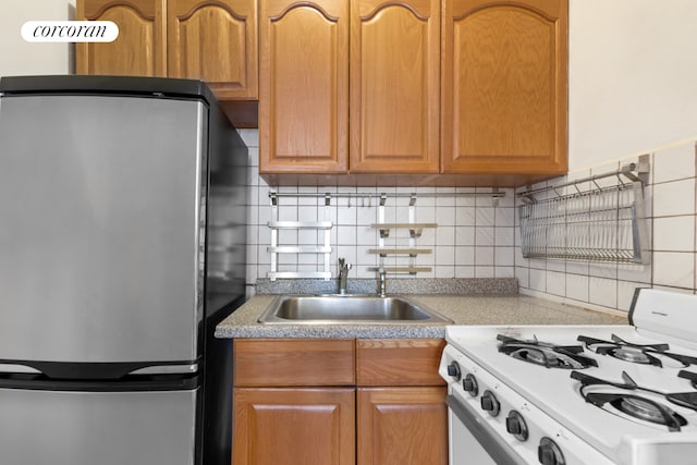 kitchen featuring a sink, tasteful backsplash, freestanding refrigerator, light countertops, and white range with gas stovetop