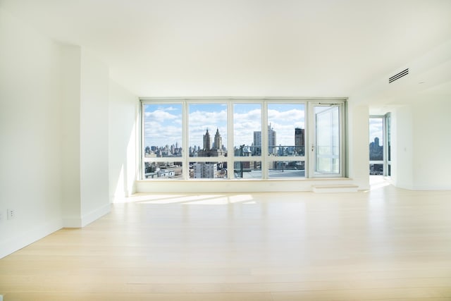 empty room with a view of city, baseboards, wood finished floors, and visible vents