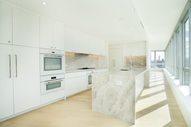 kitchen with a sink, double oven, light wood-style flooring, black stovetop, and tasteful backsplash