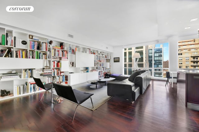 living area with wall of books, visible vents, expansive windows, and wood finished floors