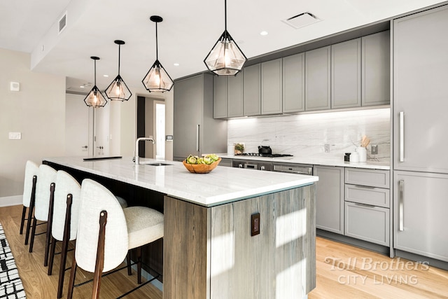 kitchen with visible vents, gray cabinetry, light stone countertops, decorative backsplash, and a sink