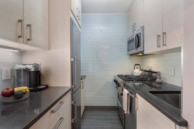 kitchen featuring dark countertops, high end appliances, backsplash, and a sink