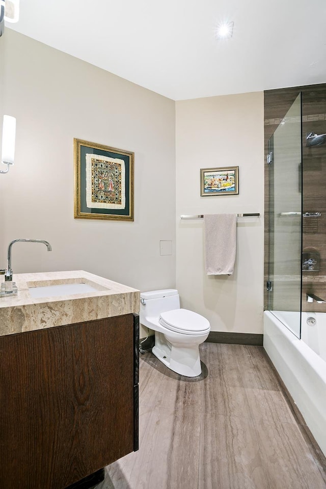 bathroom with vanity, wood finished floors, baseboards, shower / bath combination with glass door, and toilet