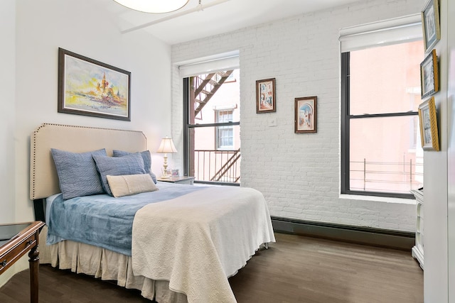 bedroom featuring a baseboard heating unit, brick wall, and dark wood-style flooring