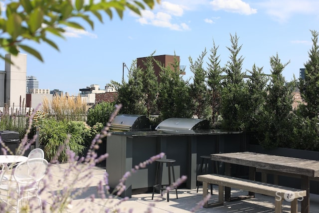 view of patio with outdoor dining space, exterior kitchen, a city view, and fence