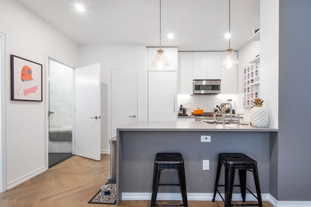 kitchen featuring a breakfast bar, a sink, stainless steel microwave, backsplash, and white cabinetry