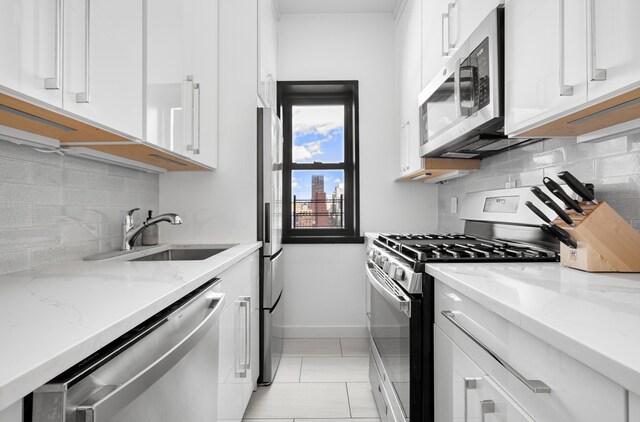 357 E 57th St Unit 16B, New York City, NY 10022 - kitchen featuring appliances with stainless steel finishes, a sink, white cabinetry, decorative backsplash, and light tile patterned flooring