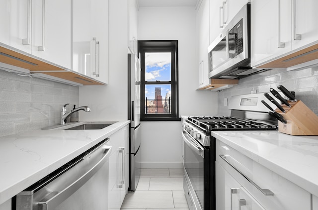 kitchen featuring a sink, light stone counters, tasteful backsplash, appliances with stainless steel finishes, and white cabinets