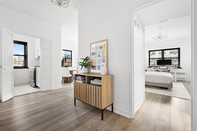 corridor featuring baseboards, light wood finished floors, radiator heating unit, crown molding, and a notable chandelier