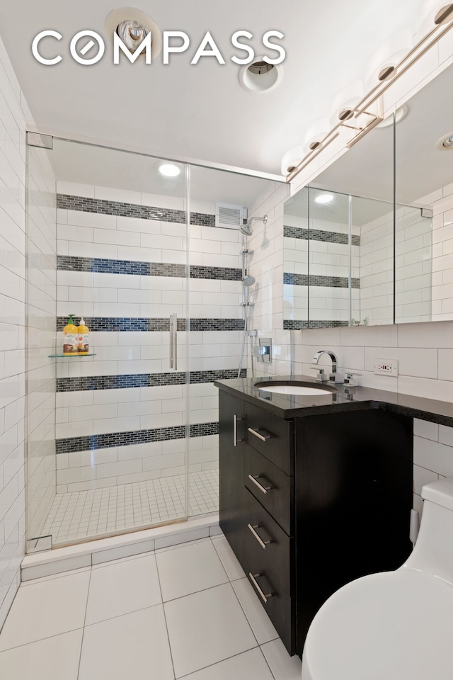 full bath with tile patterned floors, toilet, a stall shower, tile walls, and vanity