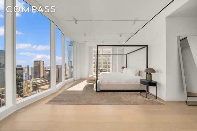 bedroom featuring a view of city, rail lighting, wood finished floors, and expansive windows