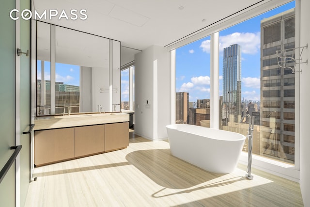 full bathroom featuring a city view, wood finished floors, a wall of windows, a soaking tub, and vanity