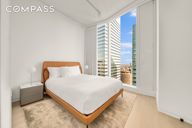 bedroom featuring multiple windows, floor to ceiling windows, wood finished floors, and rail lighting