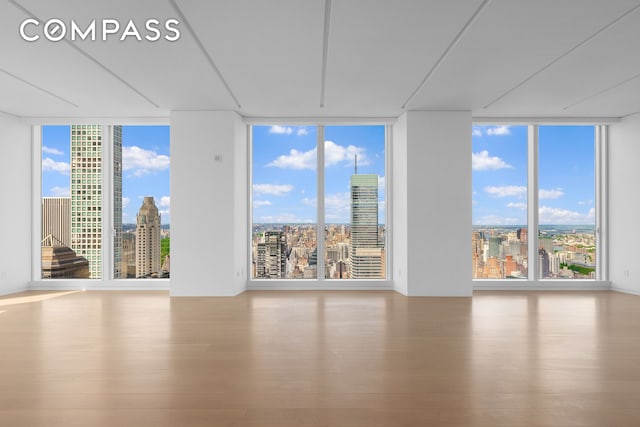 unfurnished room featuring a city view, a wall of windows, and wood finished floors