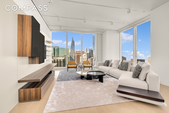 living room featuring rail lighting, a view of city, a wall of windows, and light wood-style floors