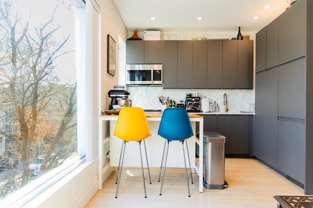 kitchen featuring light wood finished floors, stainless steel microwave, decorative backsplash, gray cabinets, and modern cabinets