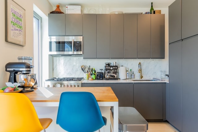 kitchen featuring a sink, tasteful backsplash, appliances with stainless steel finishes, and gray cabinets