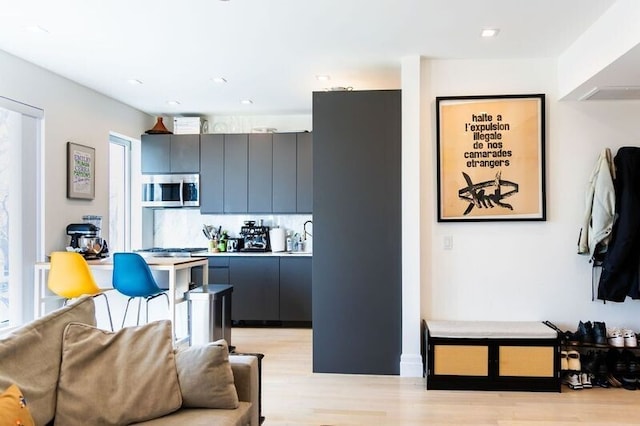 kitchen featuring stainless steel microwave, backsplash, light countertops, light wood-style flooring, and modern cabinets