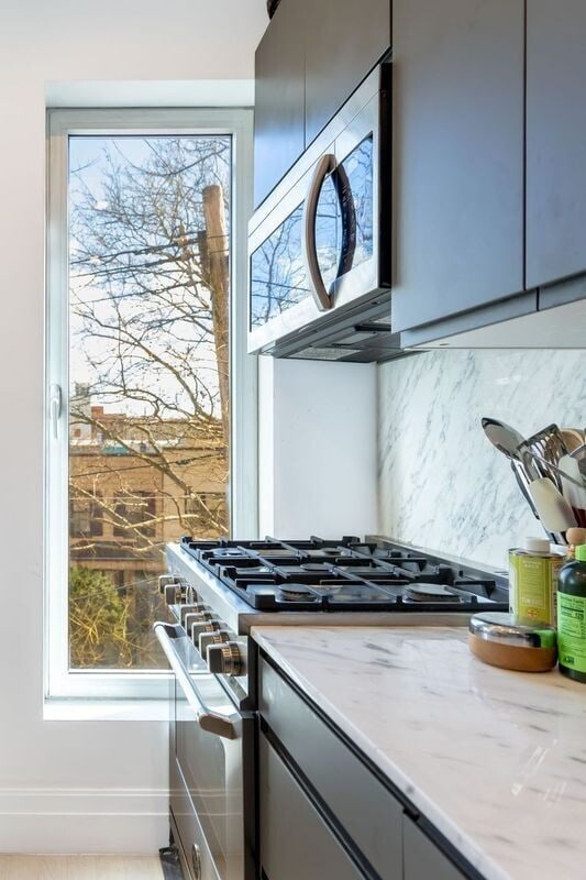 room details with backsplash, gray cabinets, stainless steel appliances, and light stone counters