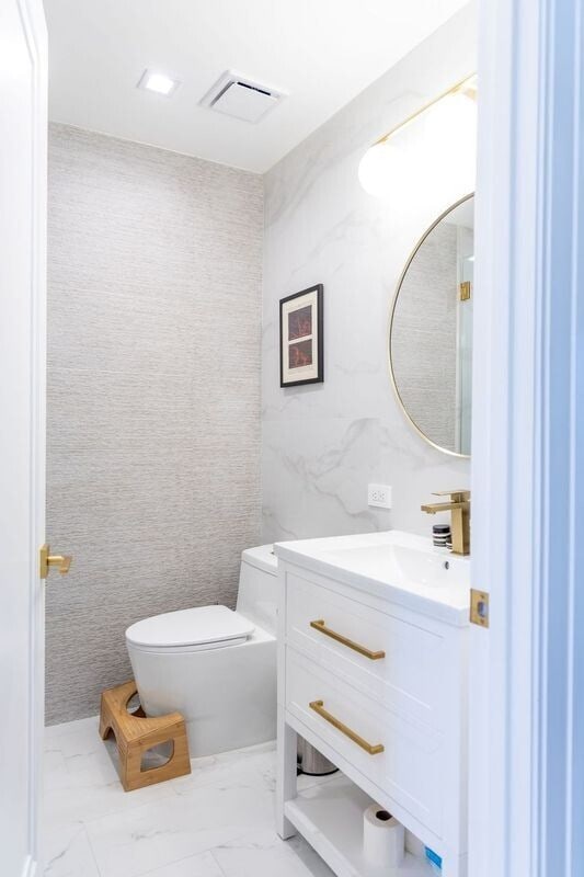 half bathroom with visible vents, toilet, vanity, marble finish floor, and tile walls