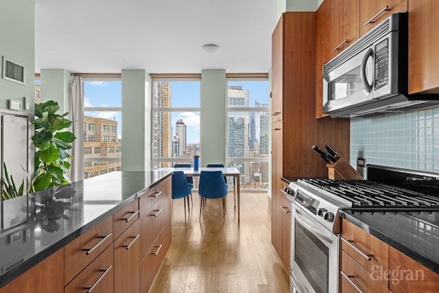 kitchen with brown cabinetry, backsplash, stainless steel appliances, and light wood-type flooring