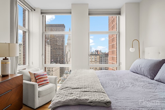 bedroom with a wall of windows, a view of city, and wood finished floors