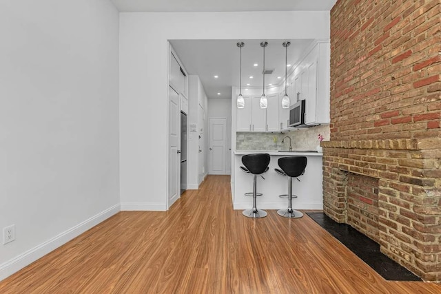 kitchen featuring light wood-type flooring, stainless steel microwave, white cabinetry, a breakfast bar area, and light countertops