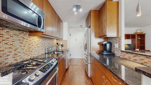 kitchen with a sink, stainless steel appliances, light wood-style floors, brown cabinets, and backsplash