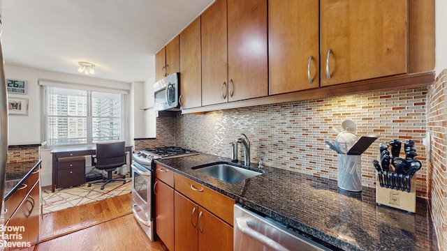 kitchen with light wood finished floors, backsplash, brown cabinetry, stainless steel appliances, and a sink