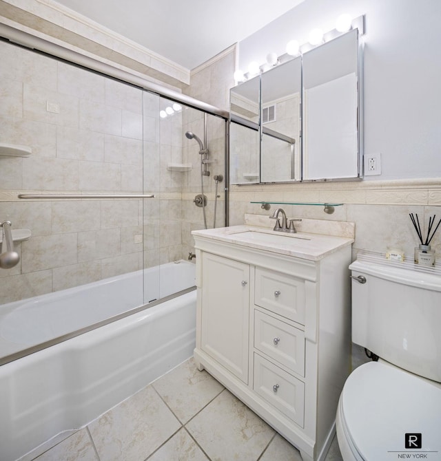 full bath with toilet, tile walls, vanity, and shower / bath combination with glass door