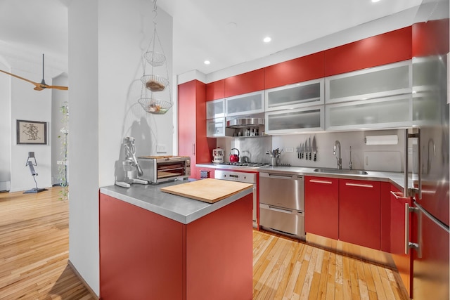 kitchen with a sink, stainless steel countertops, light wood-style floors, appliances with stainless steel finishes, and red cabinets