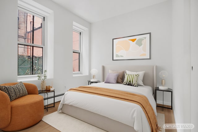 bedroom with a baseboard heating unit, baseboards, and wood finished floors