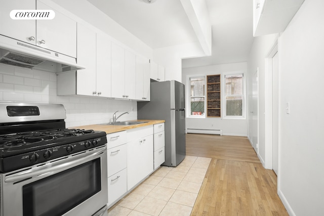 kitchen with under cabinet range hood, a sink, backsplash, a baseboard radiator, and stainless steel range with gas stovetop