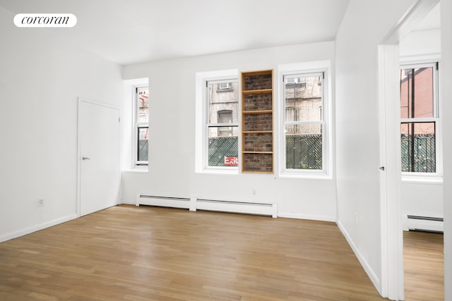 spare room with baseboards, light wood-style floors, visible vents, and a baseboard radiator