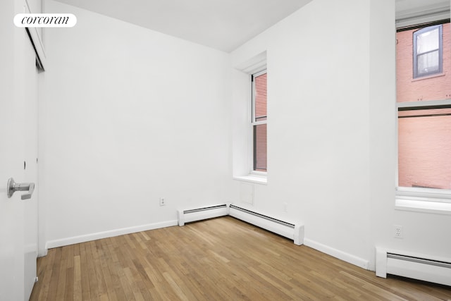 empty room featuring baseboard heating, baseboards, and wood-type flooring