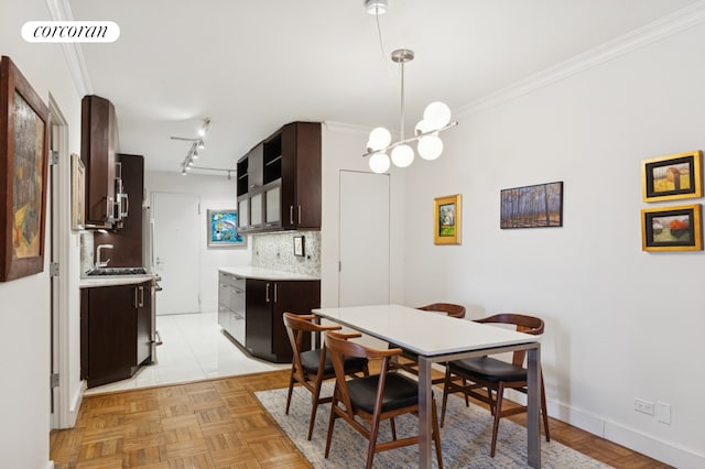 dining area with rail lighting, baseboards, a notable chandelier, and crown molding