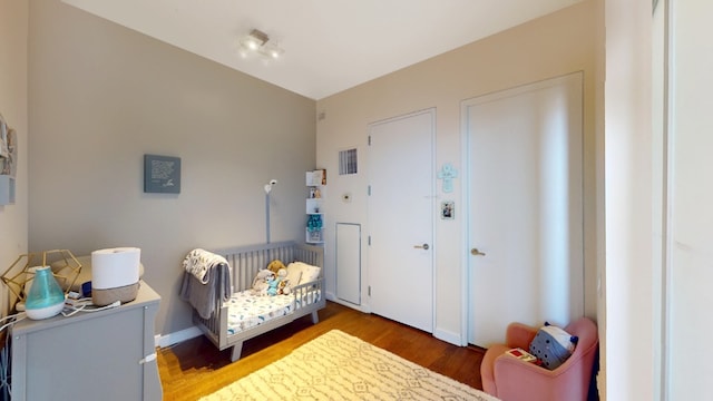 bedroom featuring visible vents, a crib, baseboards, and wood finished floors