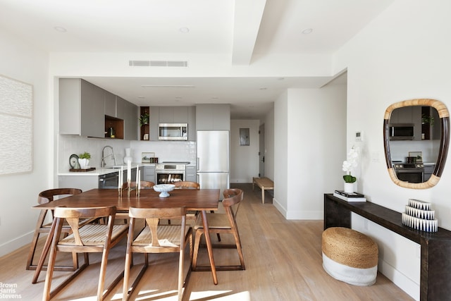 dining area featuring visible vents, baseboards, light wood-style floors, and beam ceiling