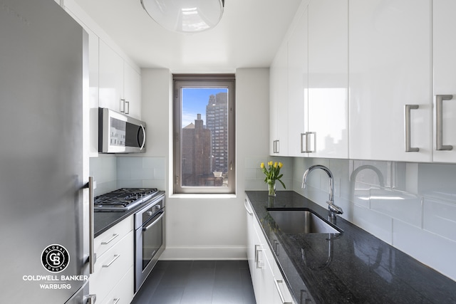 kitchen with appliances with stainless steel finishes, a sink, baseboards, dark stone countertops, and white cabinets