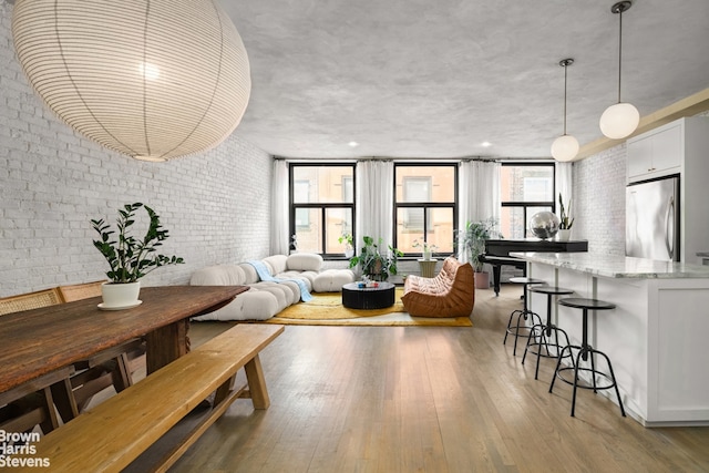 dining space with a wall of windows, light wood-style flooring, and brick wall