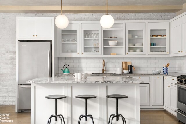 kitchen featuring wood finished floors, light stone countertops, a sink, stainless steel appliances, and white cabinetry