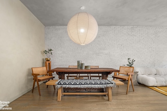 dining room featuring wood finished floors, baseboards, and brick wall