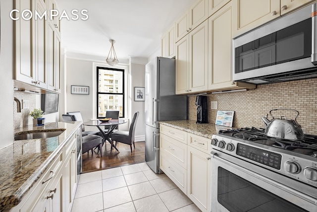 kitchen with light stone counters, light tile patterned floors, a sink, ornamental molding, and stainless steel appliances