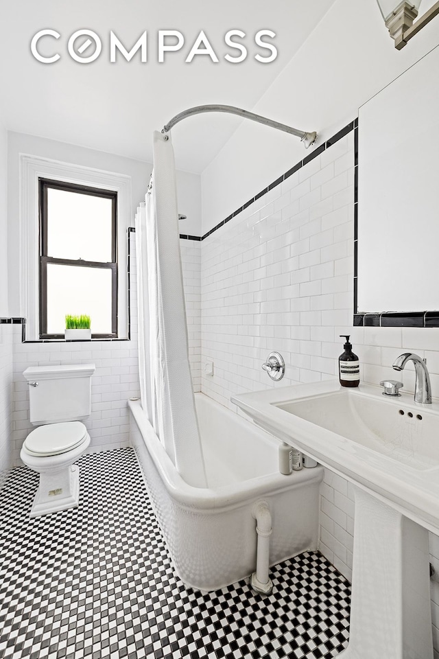 bathroom with tile walls, toilet, shower / bath combo with shower curtain, and tile patterned floors