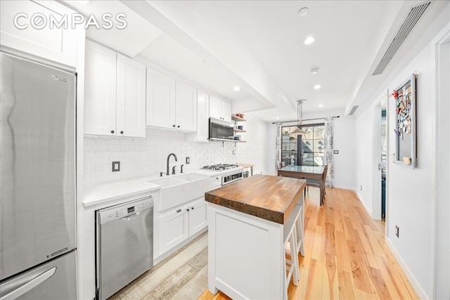 kitchen with a sink, light wood-style floors, appliances with stainless steel finishes, wood counters, and white cabinetry