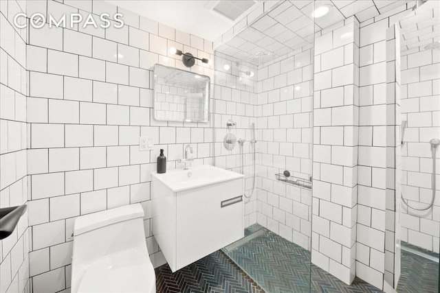 bathroom featuring vanity, tile walls, toilet, and tiled shower