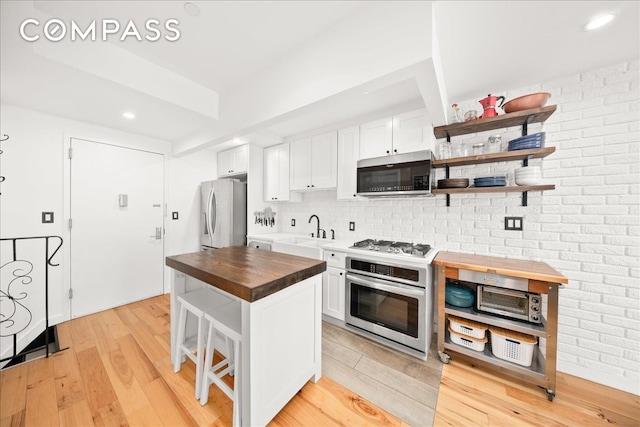 kitchen featuring a sink, wood counters, stainless steel appliances, light wood-style floors, and white cabinets