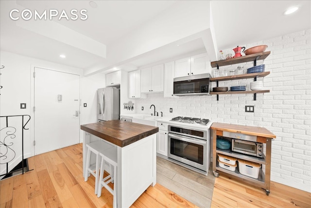 kitchen featuring a sink, white cabinets, wooden counters, and stainless steel appliances