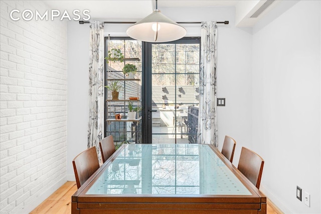 dining space with baseboards, wood finished floors, and brick wall