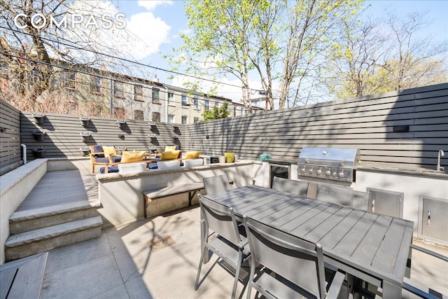 view of patio with outdoor dining space, exterior kitchen, a fenced backyard, and a grill